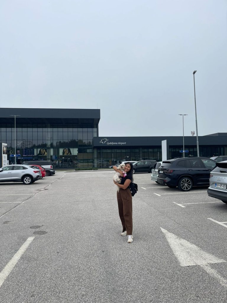 A woman joyfully holds her white Maltese dog Luna at Ljubljana Airport after their successful pet relocation to Bosnia with Pet Travel Indo, a trusted pet travel partner.
